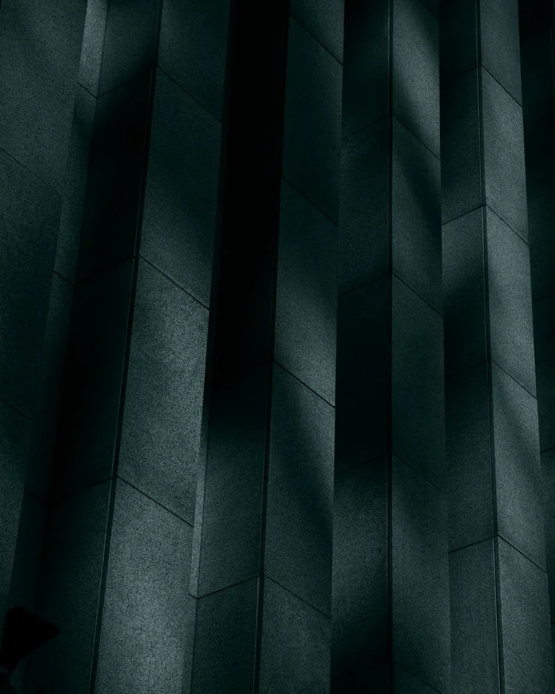 Tall concrete wall panels catch narrow bands of light in a minimalist architectural scene.