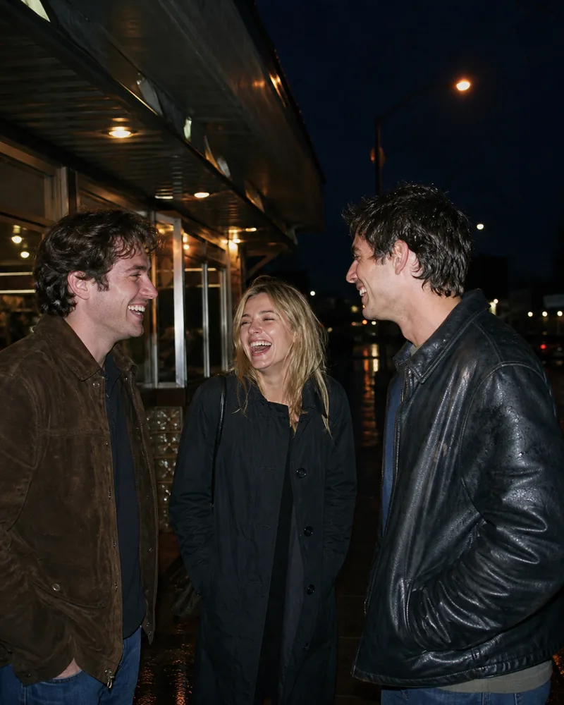 Three friends laugh together outdoors at night under direct camera flash.