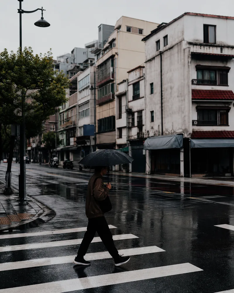 The rainy umbrella street after a muted analog film treatment with softer color and restrained contrast.